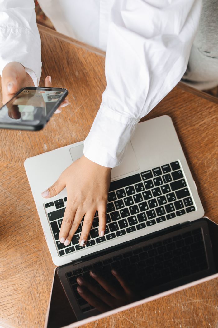 who-we-are Hands typing on a laptop while holding a smartphone, showing a multitasking work environment.